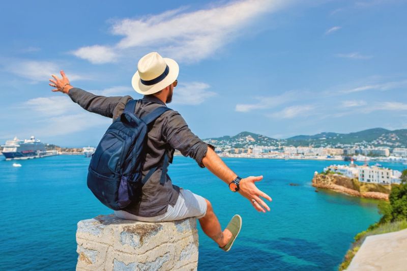 male standing on a mountain top looking out to sea with arms out